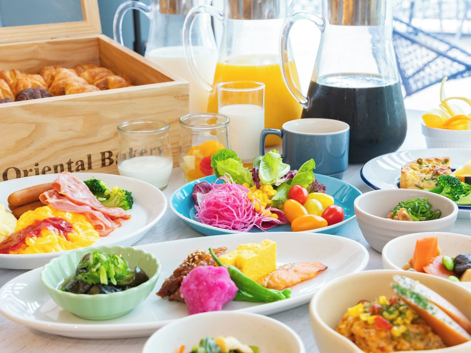 Un bufé de desayuno con diversos platos, bebidas y una caja de madera con pasteles.
