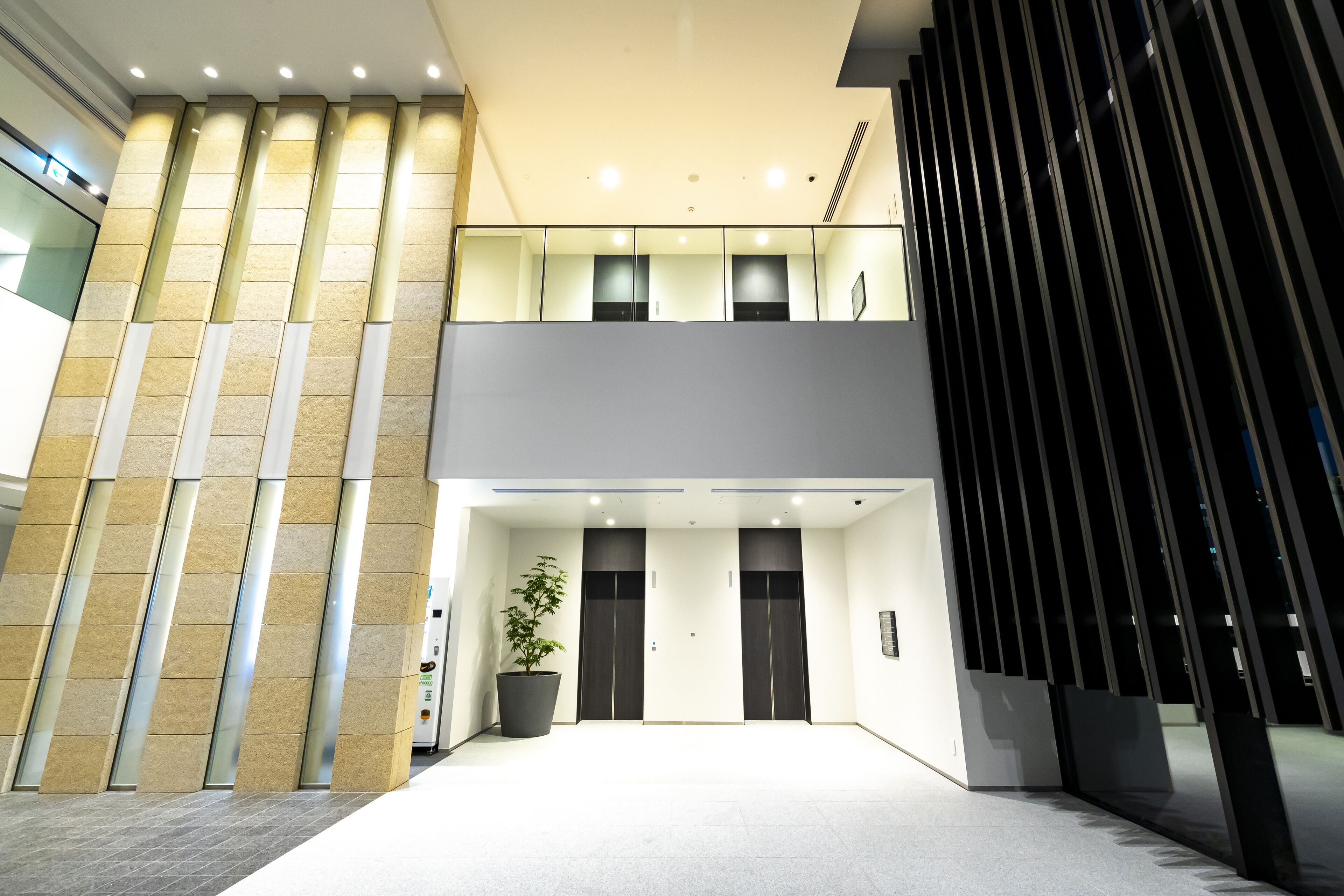 A modern hotel lobby with a central reception desk, a large potted plant, and a staircase leading to an upper floor.