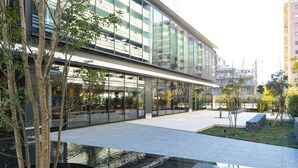 Un bâtiment moderne doté de grandes fenêtres en verre, d’une cour intérieure avec des arbres et d’un élément décoratif aquatique.