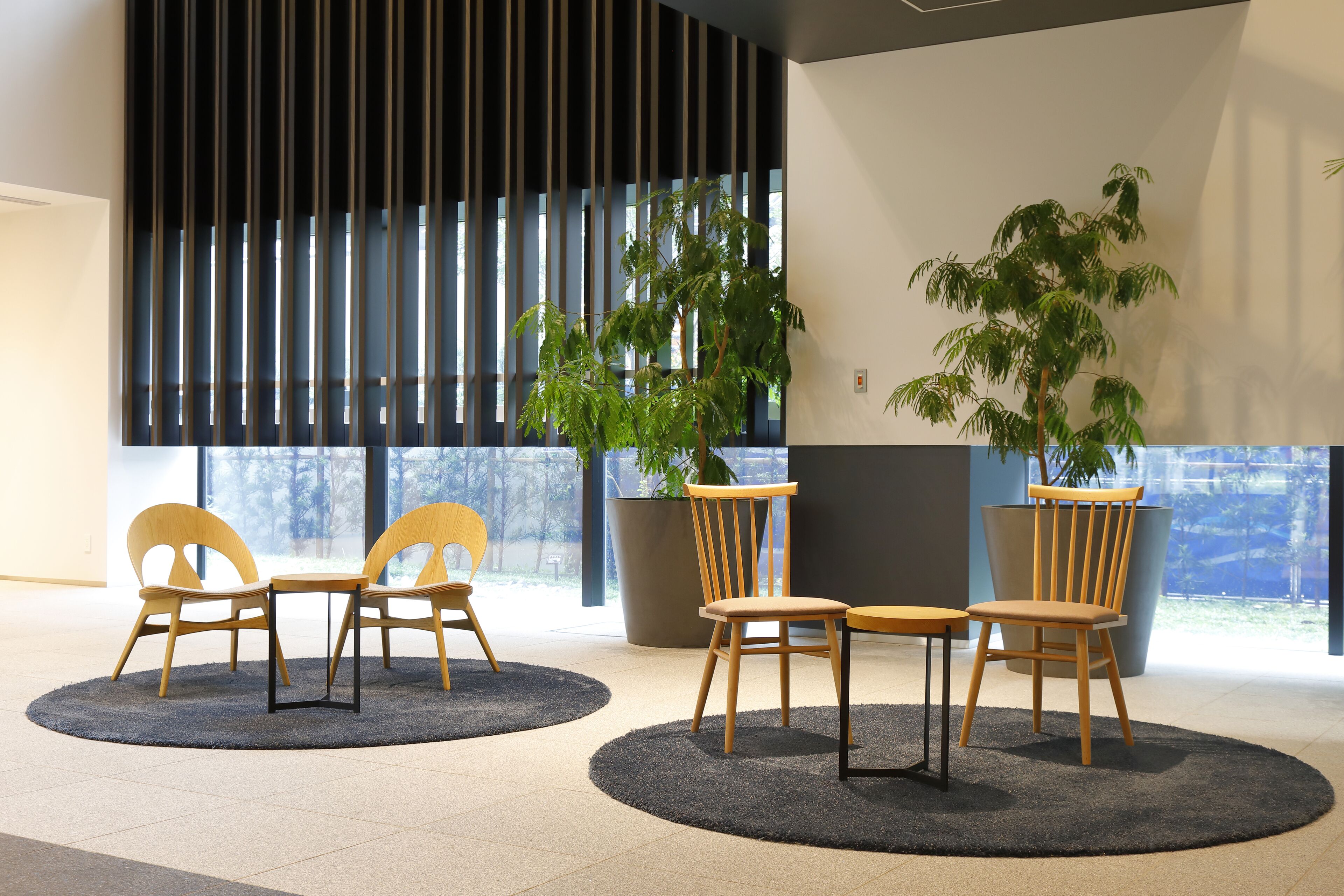 A modern indoor space with a circular seating area, large windows, and potted plants.