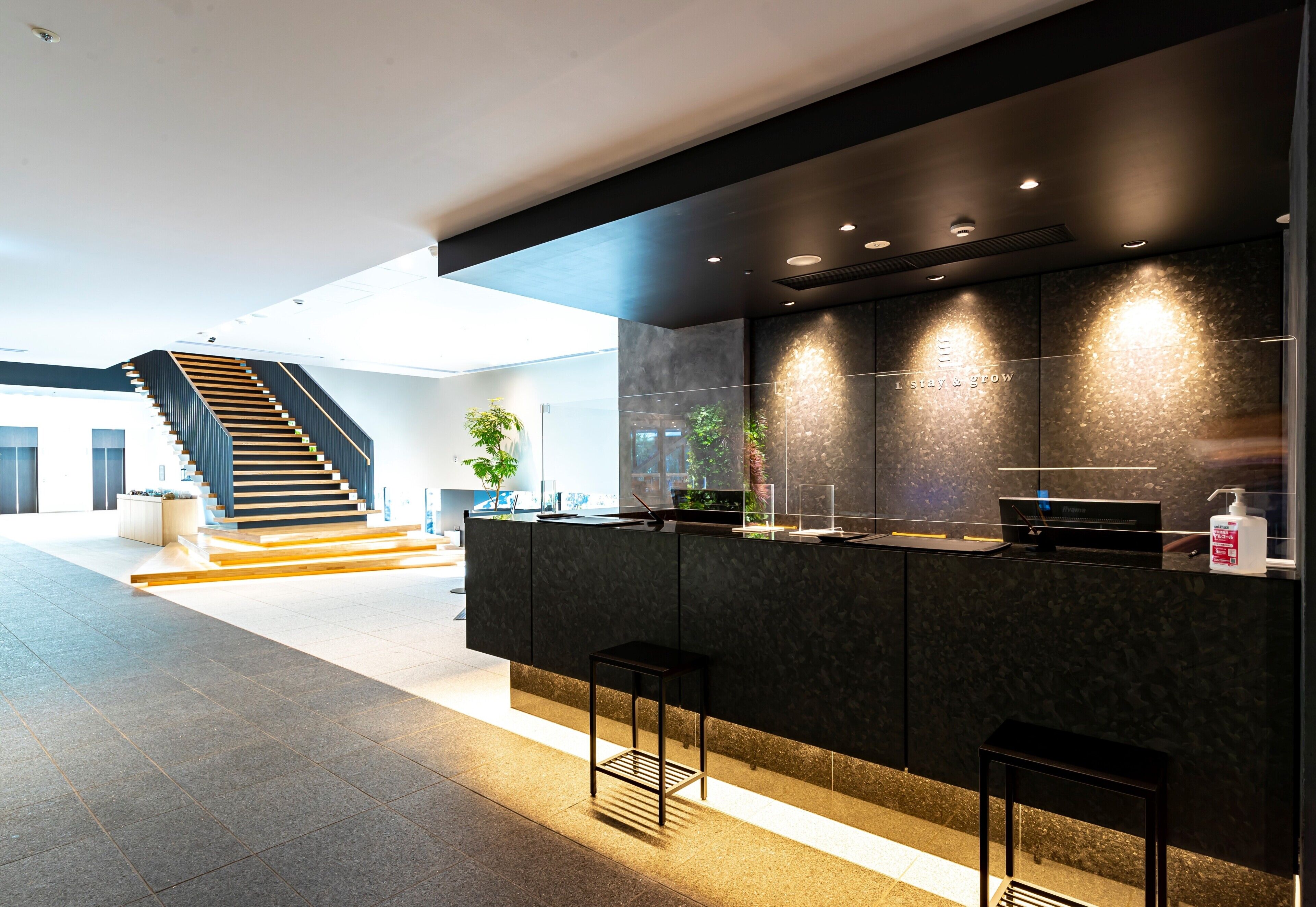 Eine moderne Küche mit dunkler Arbeitsplatte, Barhocker und einer Treppe im Hintergrund.