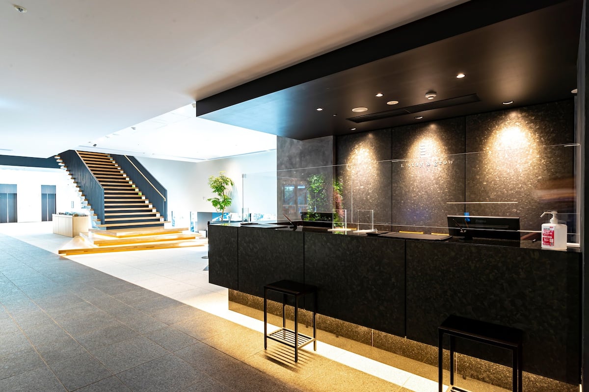 A modern kitchen with a dark countertop, bar stools, and a staircase in the background.