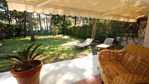A covered patio with a wicker sofa, two lounge chairs, and a potted plant. - Seaside Villa With Private Garden (Lignano Sabbiadoro)