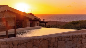 A stone building with a pool overlooking the sea at sunset.