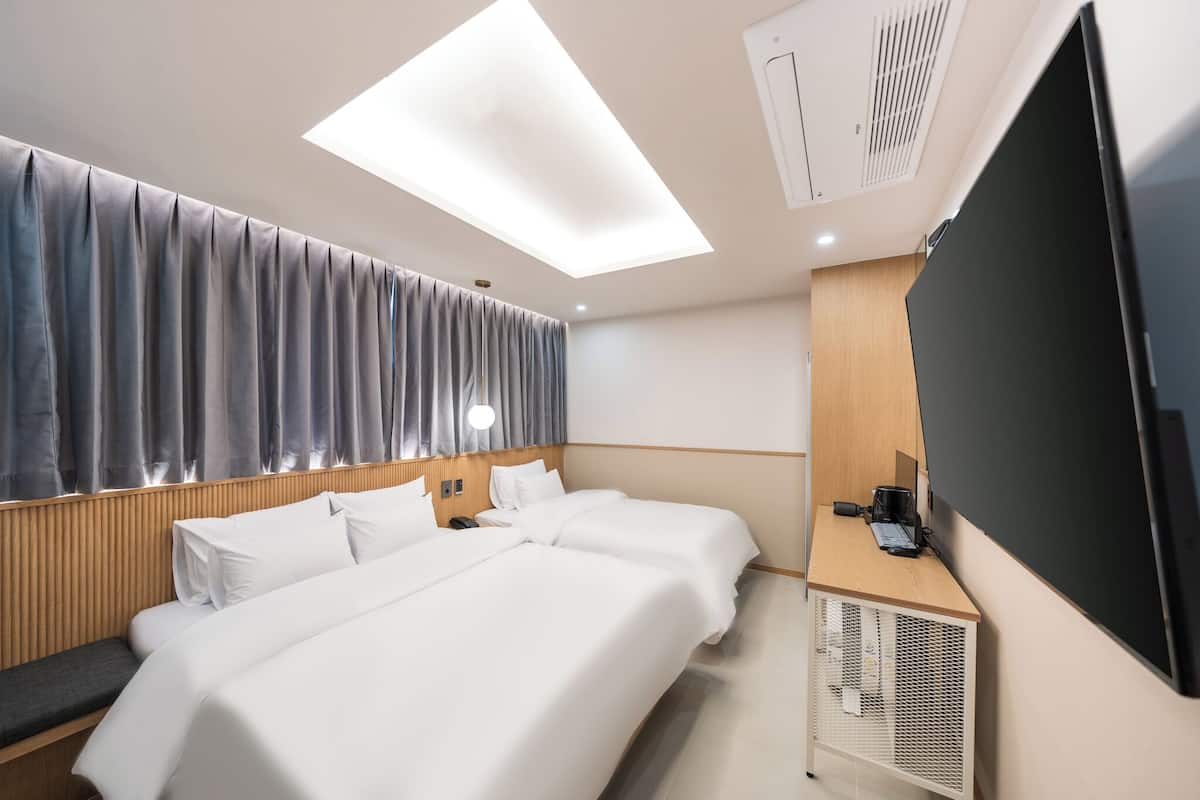 A hotel room with a large bed, a desk with a flat-screen TV, a ceiling light, and a ventilation unit.