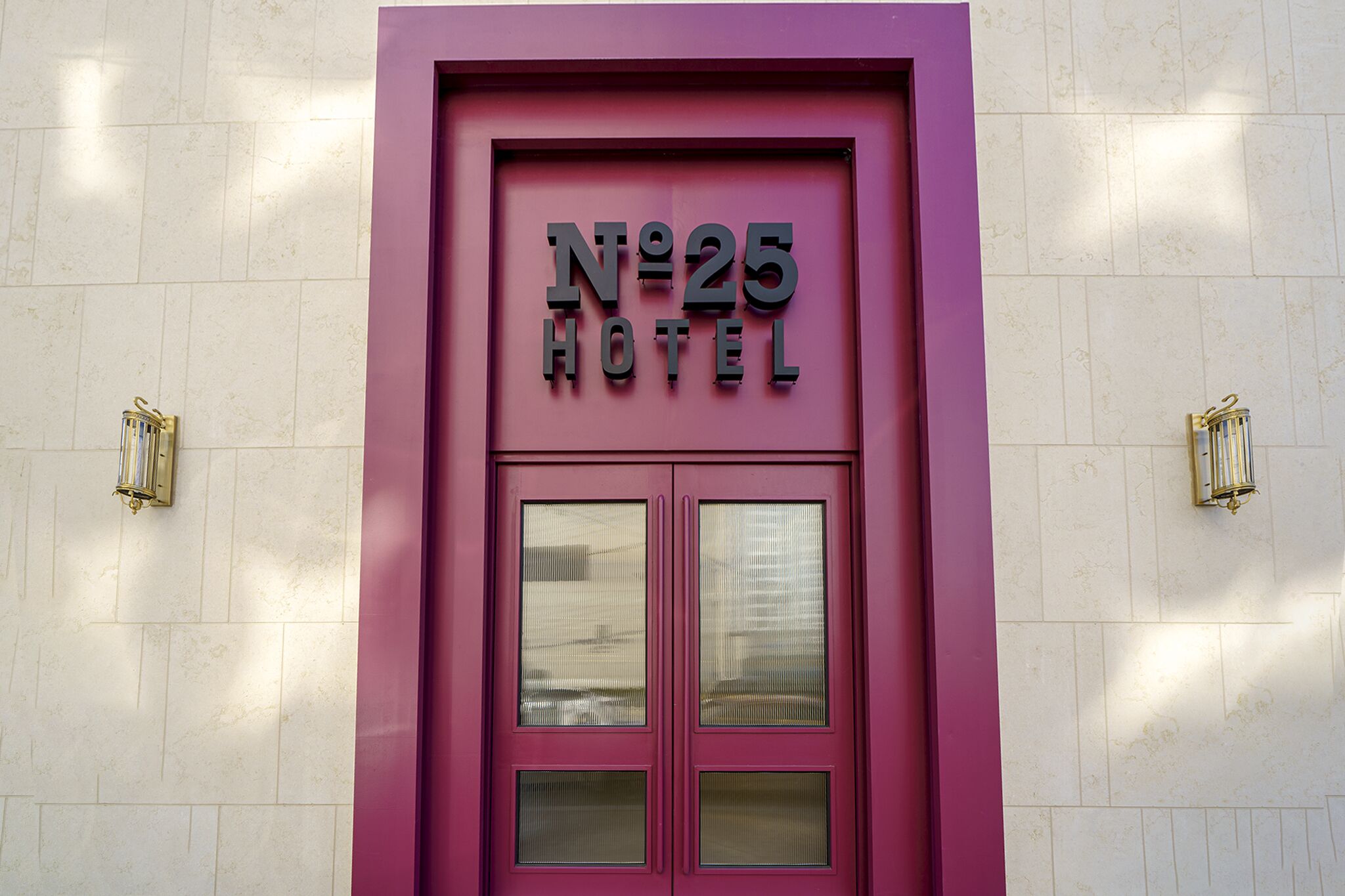 Entrada de un hotel con fachada rosa y un letrero que dice "N°25 HOTEL".