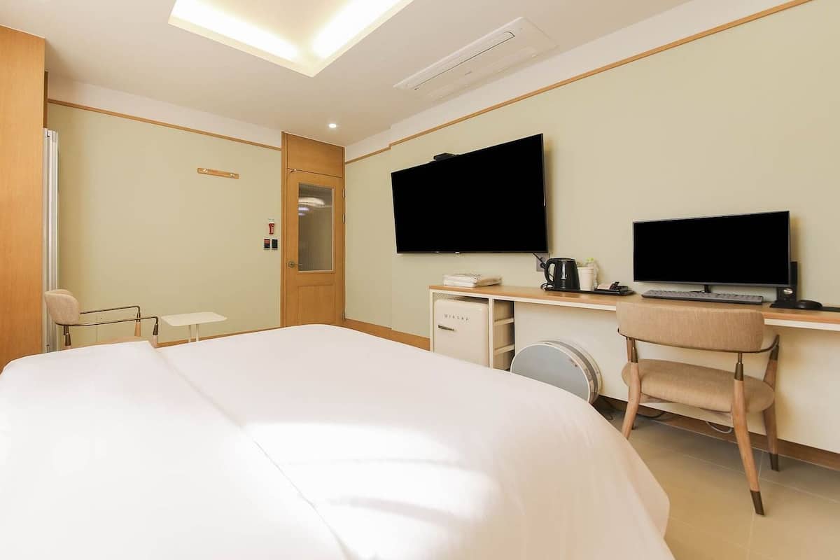 A hotel room with a bed, a desk, a chair, a television, and a mirror.