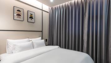 A modern hotel room with a neatly made bed, a large window with curtains, and two framed artworks on the wall.