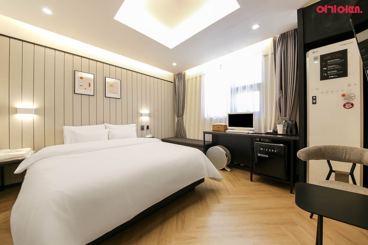 A hotel room with a bed, a desk with a computer, a chair, and a window with curtains.
