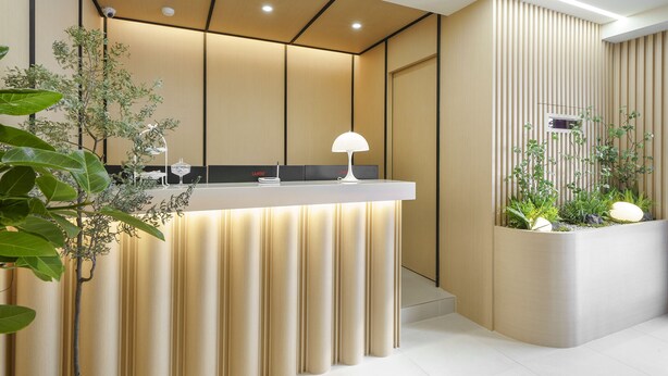 A reception desk with a modern design, featuring a light-colored counter, a white lamp, and a potted plant. - No.25 Hotel (Gwangju)