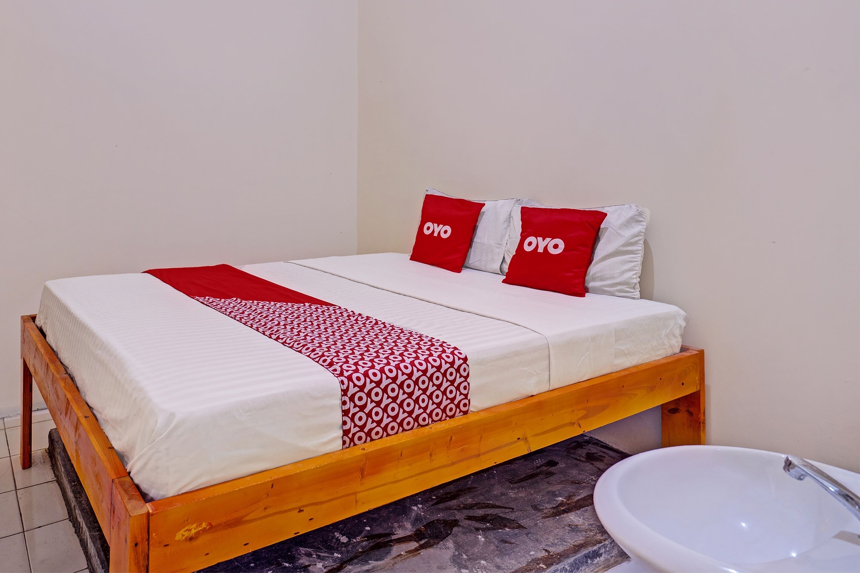 A single bed with a wooden frame, white bedding, and red and white patterned pillows.