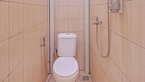 Une petite salle de bain étroite, équipée d’un WC, d’une douche et d’un porte-rouleau de papier toilette.