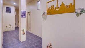 Un couloir décoré d’une œuvre d’art représentant un paysage urbain, agrémenté d’un panneau indiquant « Souriez » et de plantes en pot.