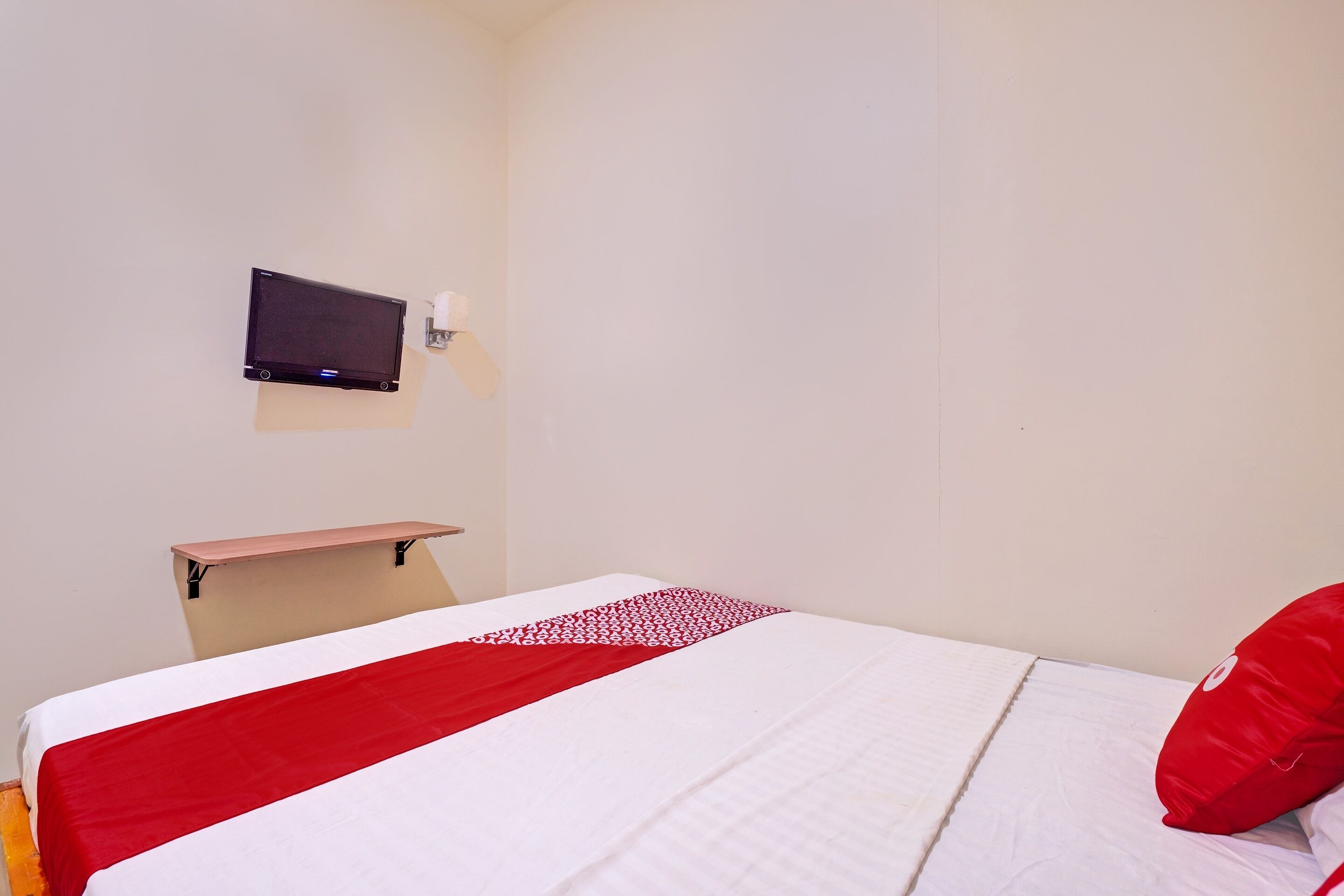 A hotel room with a bed, a flat-screen TV mounted on the wall, and a small table.