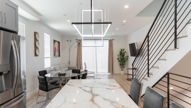 A modern kitchen with a marble island, a dining area with a glass table, and a staircase with a black railing. - MODERN 4BR TOWNHOME BUILT 2023 w/ 2-CAR GARAGE WITH EV CHARGER & 2 BALCONIES (p63) (Los Angeles)