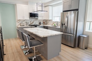 A modern kitchen with a marble countertop, stainless steel appliances, and a bar area with stools.