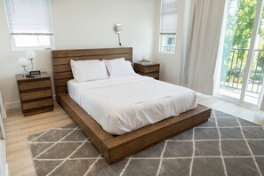 A modern bedroom with a wooden bed, bedside tables, and a view of the outdoors.