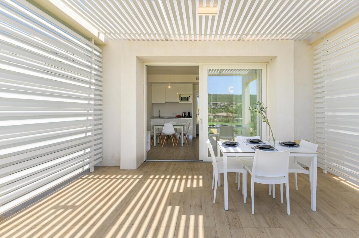 A modern dining area with a table set for four, a kitchen in the background, and a view through a glass door.