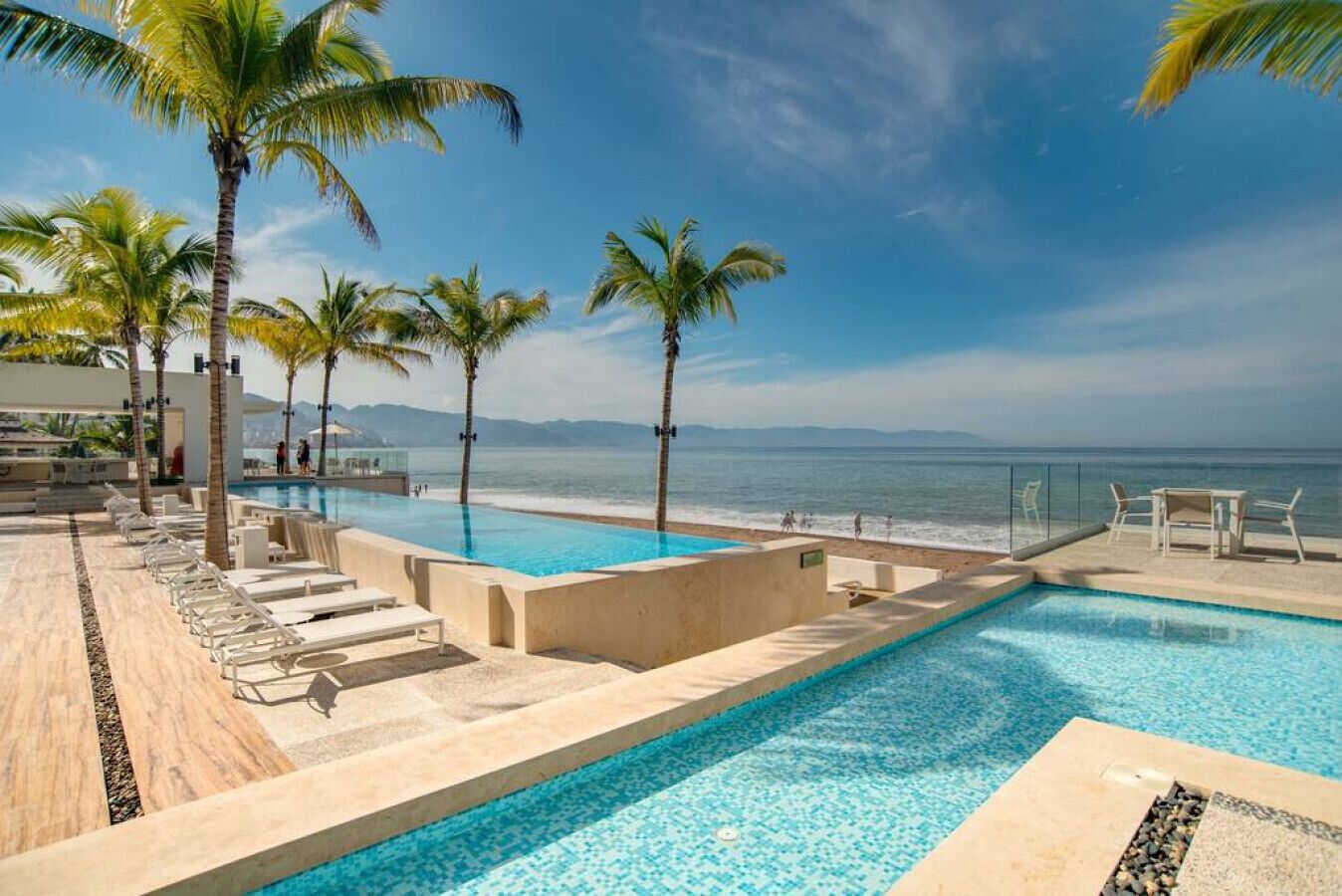 Zona de piscina con sillones de descanso, palmeras y vista al océano.