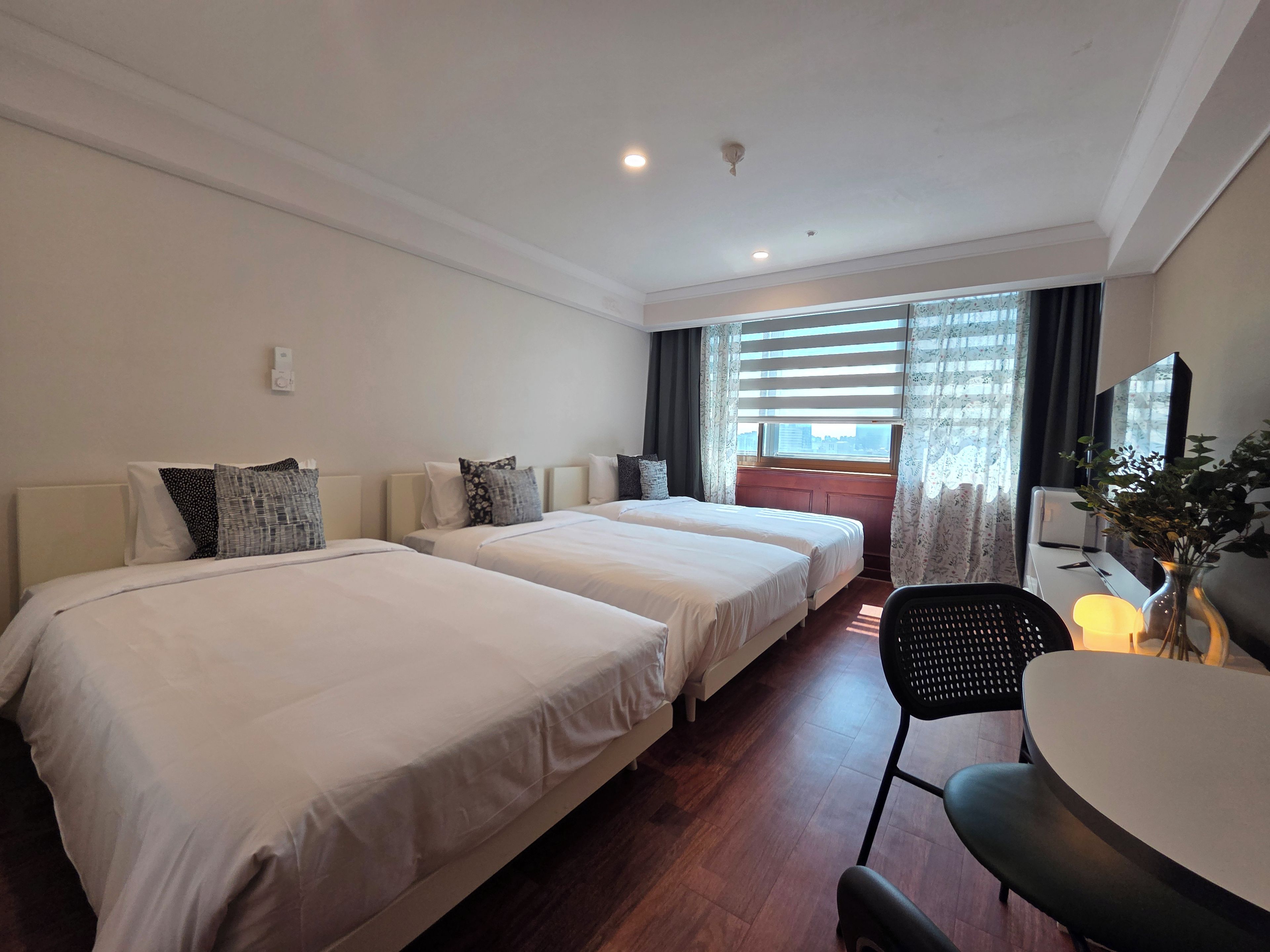 Une chambre d’hôtel avec deux lits, un bureau, une chaise, une lampe et une fenêtre avec des rideaux.