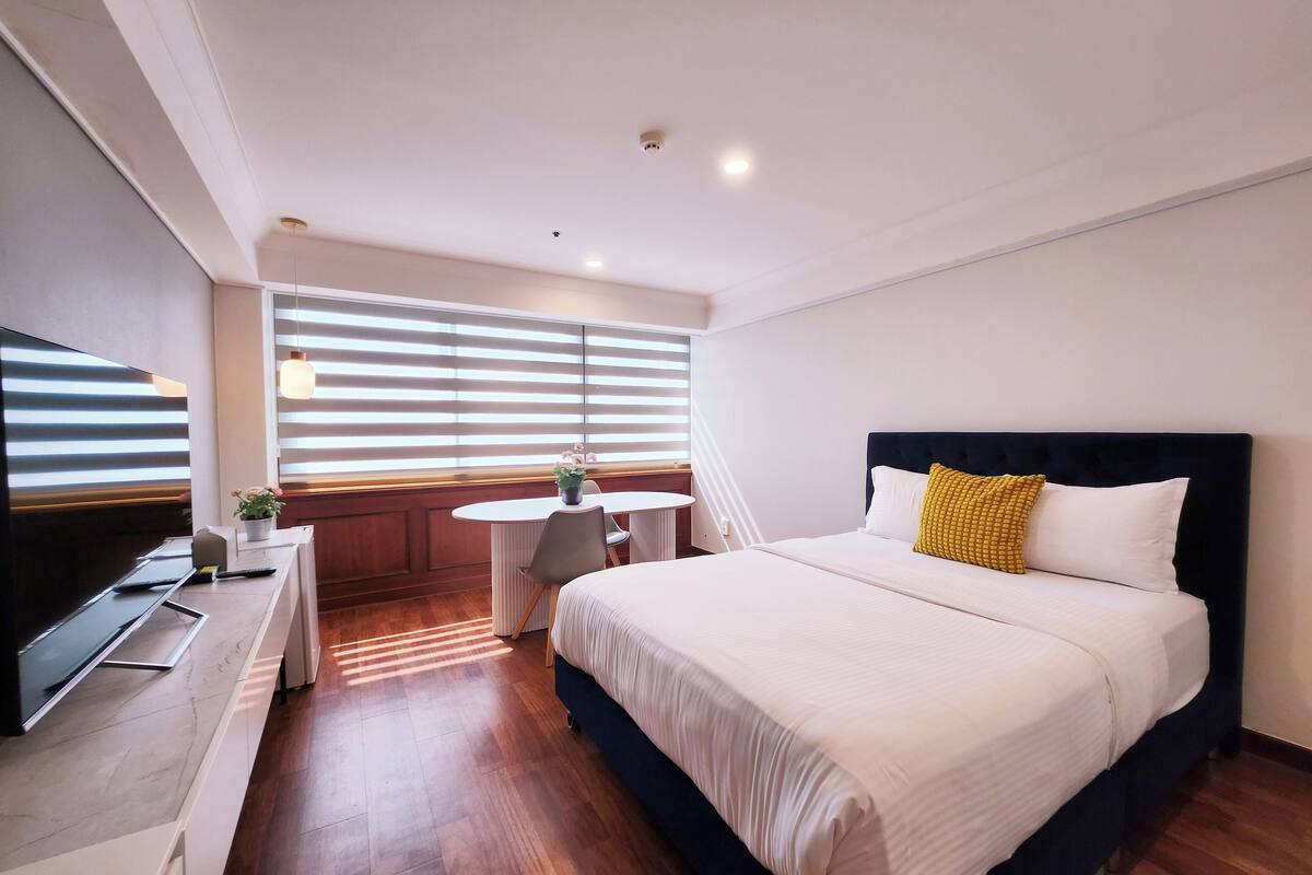 Ein modernes Hotelzimmer mit einem großen Bett, einem Fernseher, einem kleinen Esstisch und einer Topfpflanze.