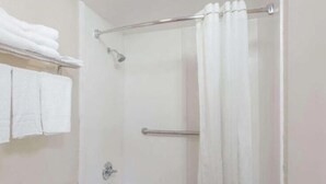 A bathroom with a shower, a toilet, and a towel rack with folded towels. - Tri City Inn (Victorville)