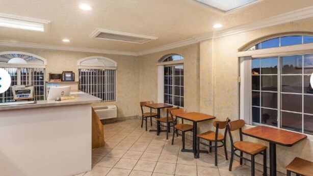 A spacious dining area with a central counter, multiple tables and chairs, and large windows providing natural light. - Tri City Inn (Victorville)