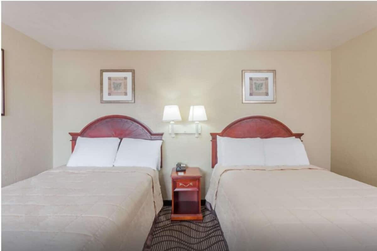 A hotel room with two beds, a nightstand with lamps, and framed pictures on the wall.