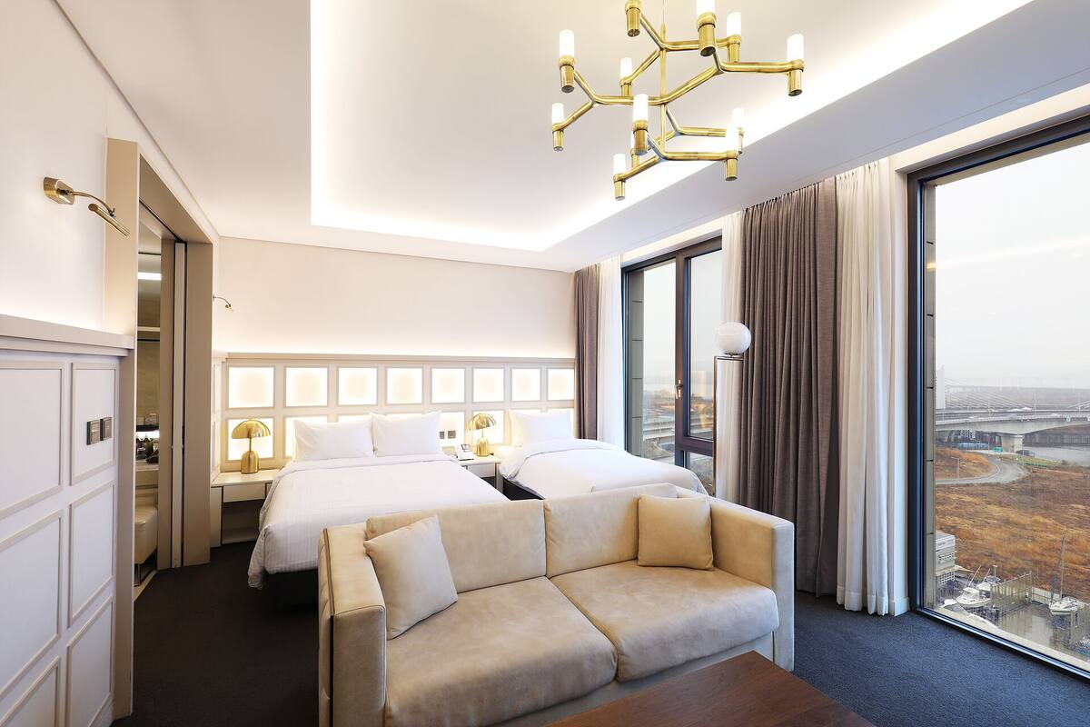 A hotel room with a large bed, a sofa, a chandelier, and a view of a bridge.