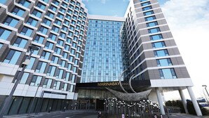 Un hotel moderno con fachada de vidrio, una entrada destacada y una escultura metálica distintiva.
