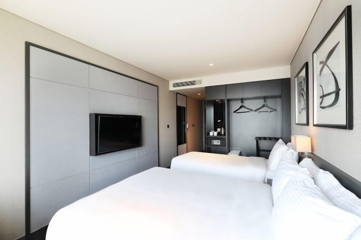 Habitación de hotel con dos camas, un televisor de pantalla plana montado en la pared, un espejo y un perchero.