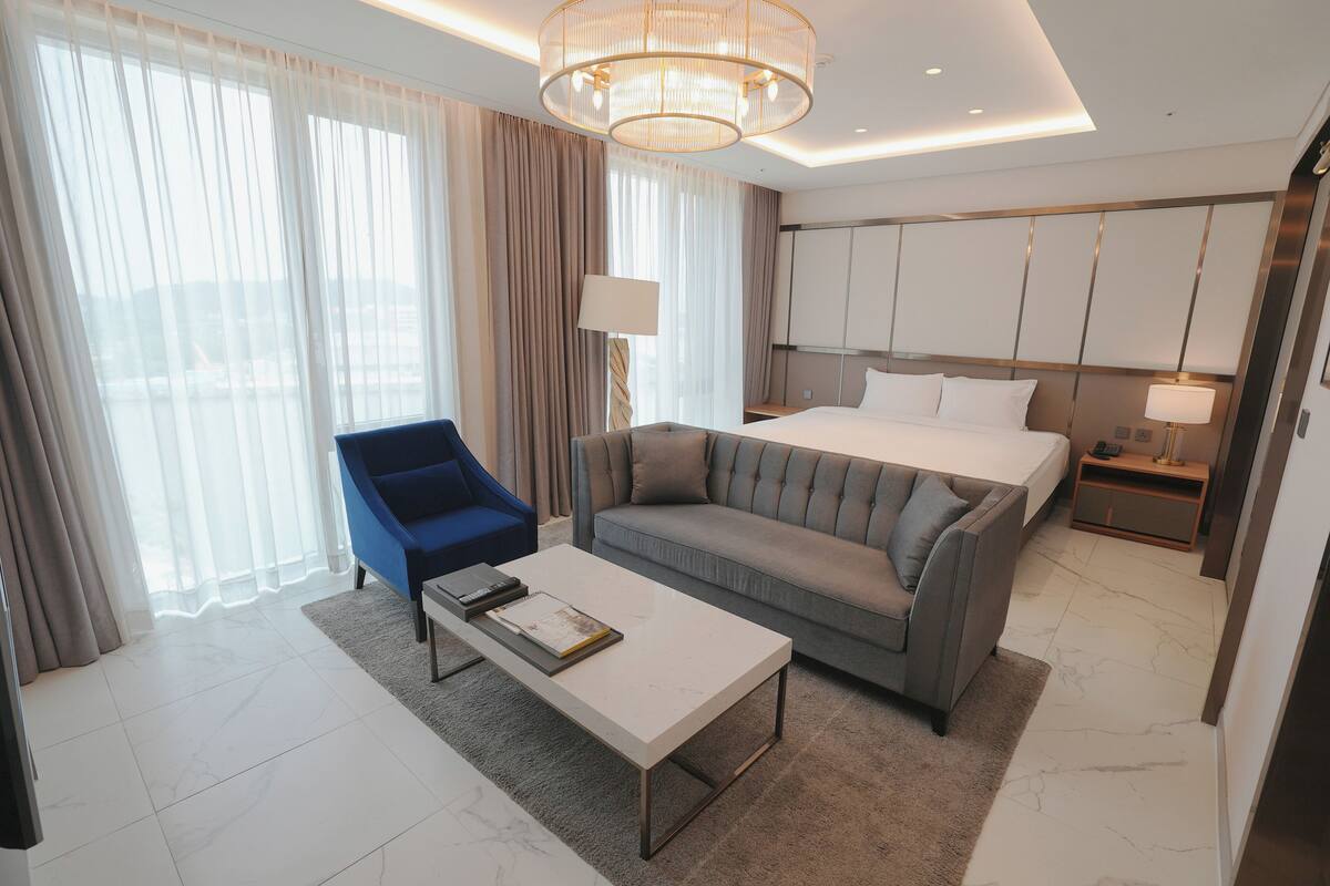 A modern hotel room with a bed, a sofa, a coffee table, and a desk.