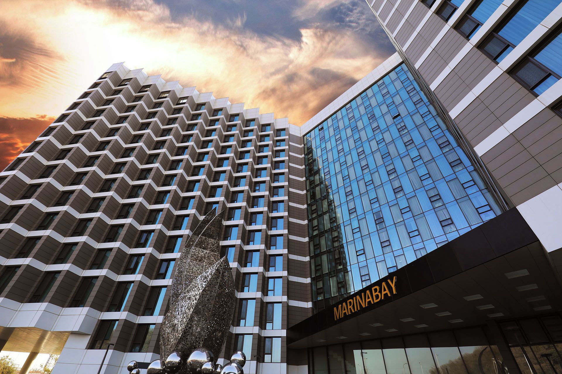 A modern building with a distinctive zigzag facade and a glass building with a 'MARINABAY' sign.