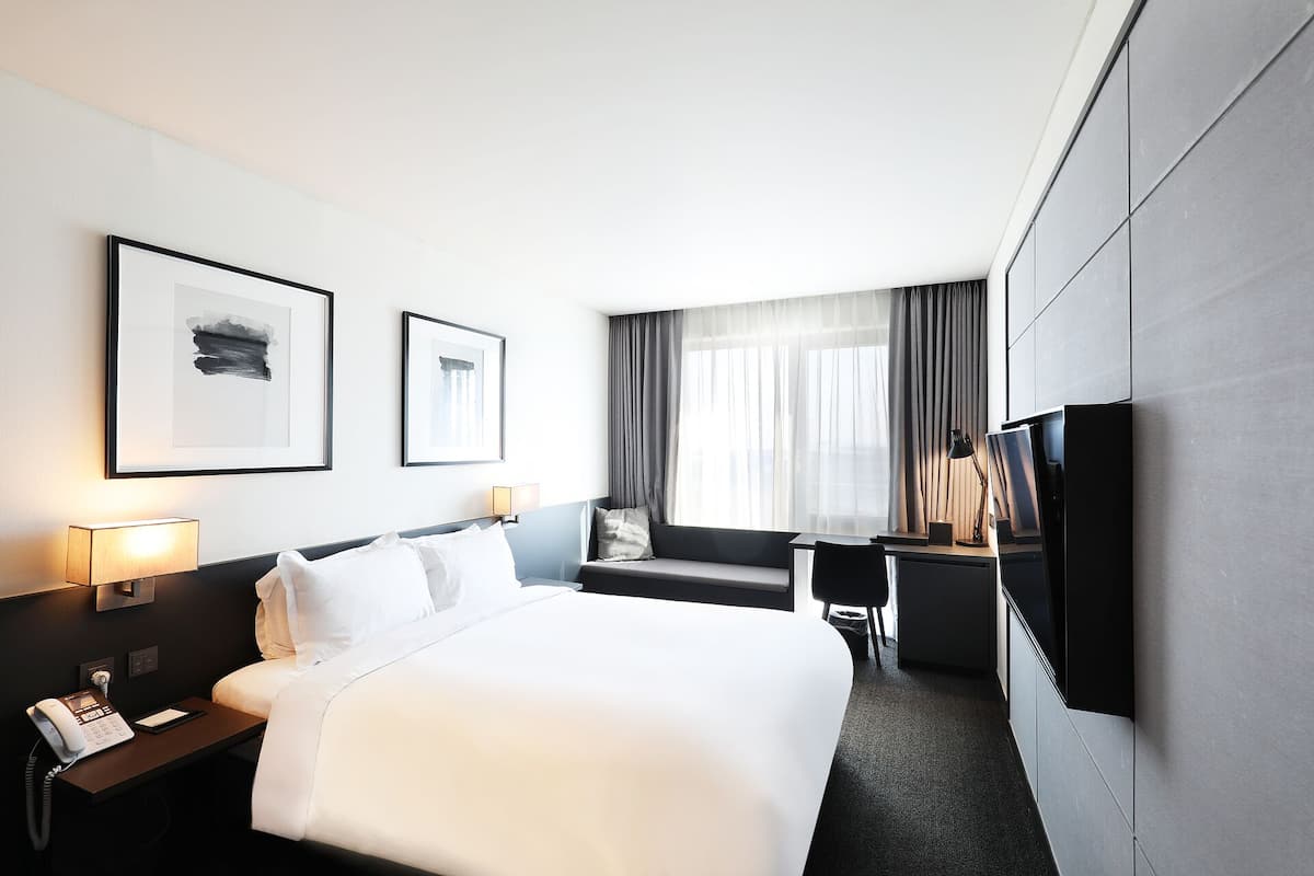 A modern hotel room with a large bed, a desk with a chair, a flat-screen TV, and two bedside lamps.