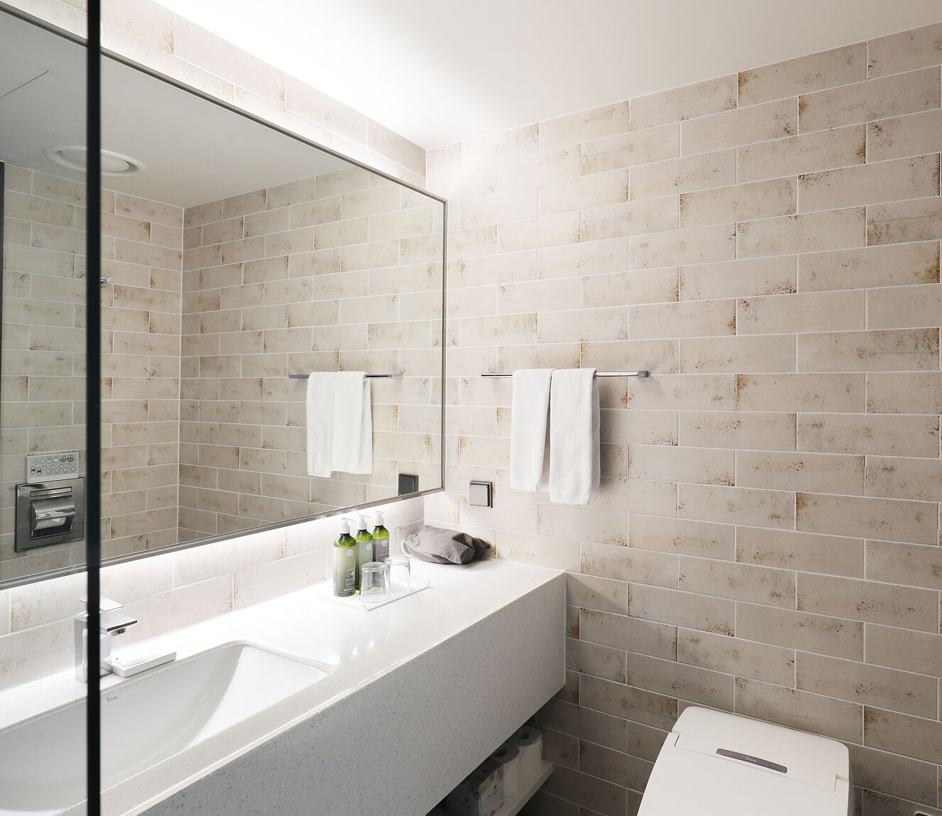 Ein modernes Badezimmer mit großem Spiegel, weißem Waschbecken und beige gefliesten Wänden.