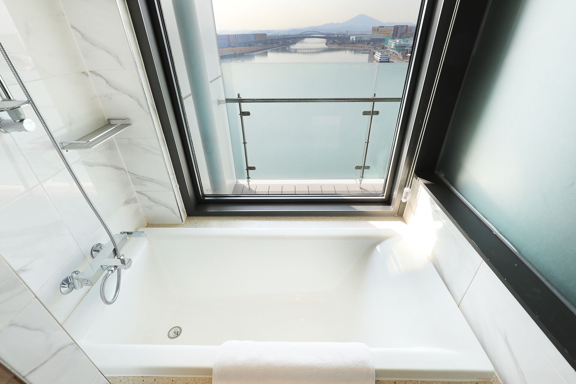 A modern bathroom with a bathtub, a glass shower enclosure, and a view of a bridge and river.