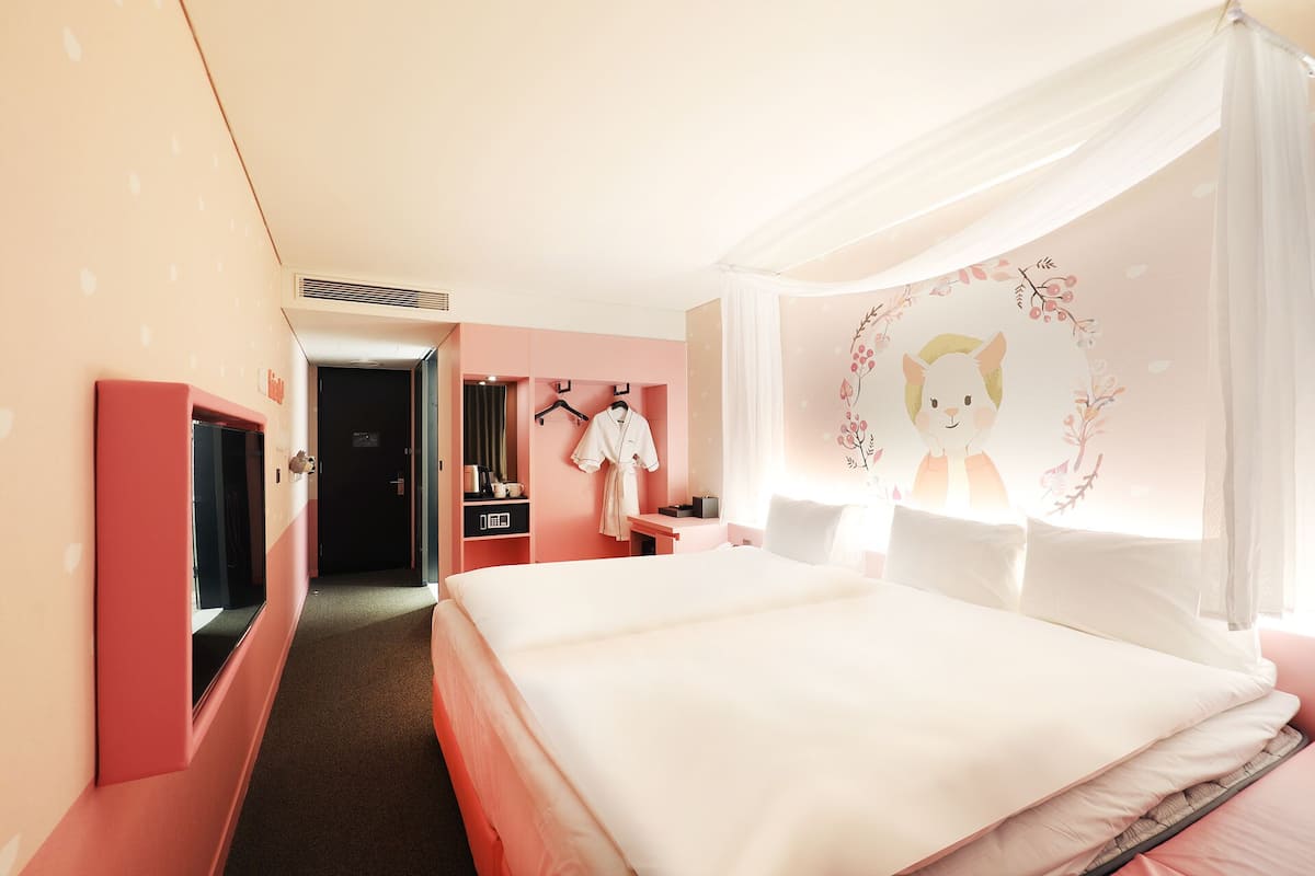 A hotel room with a bed, a wardrobe, a desk, and a mirror.