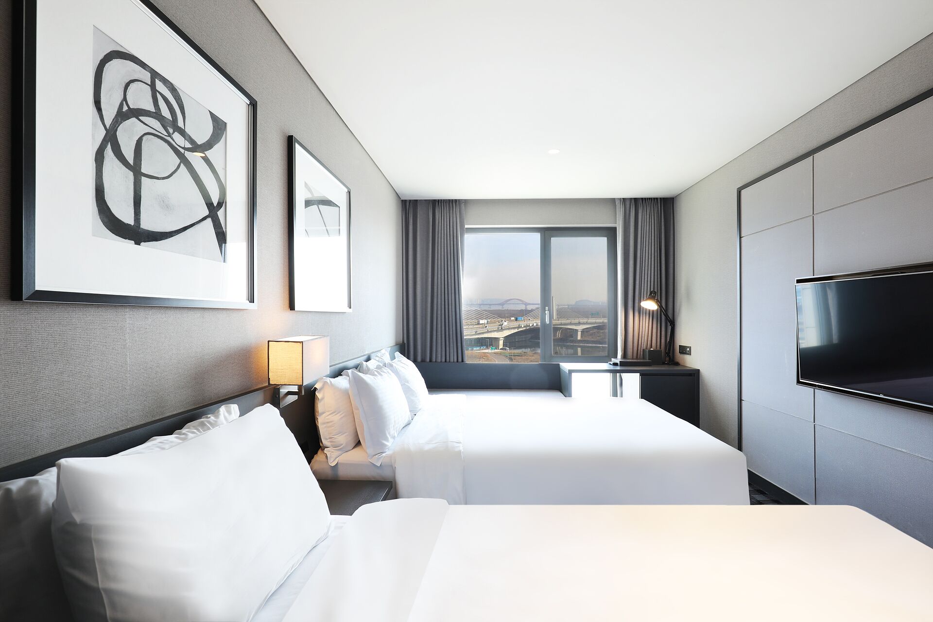 Ein Hotelzimmer mit zwei Betten, einem Fernseher und einem großen Fenster mit Blick auf die Stadt.