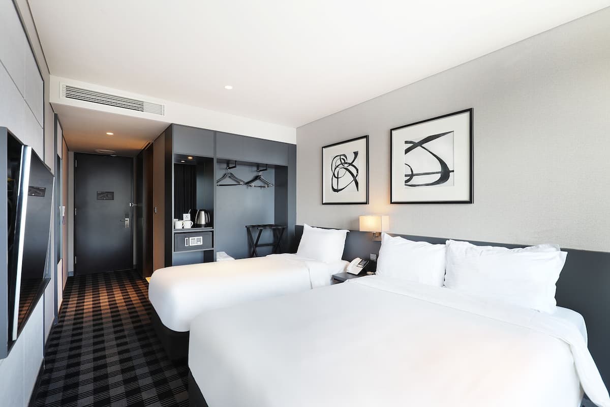 A hotel room with a large bed, a desk with a coffee maker, and two framed abstract art pieces on the wall.