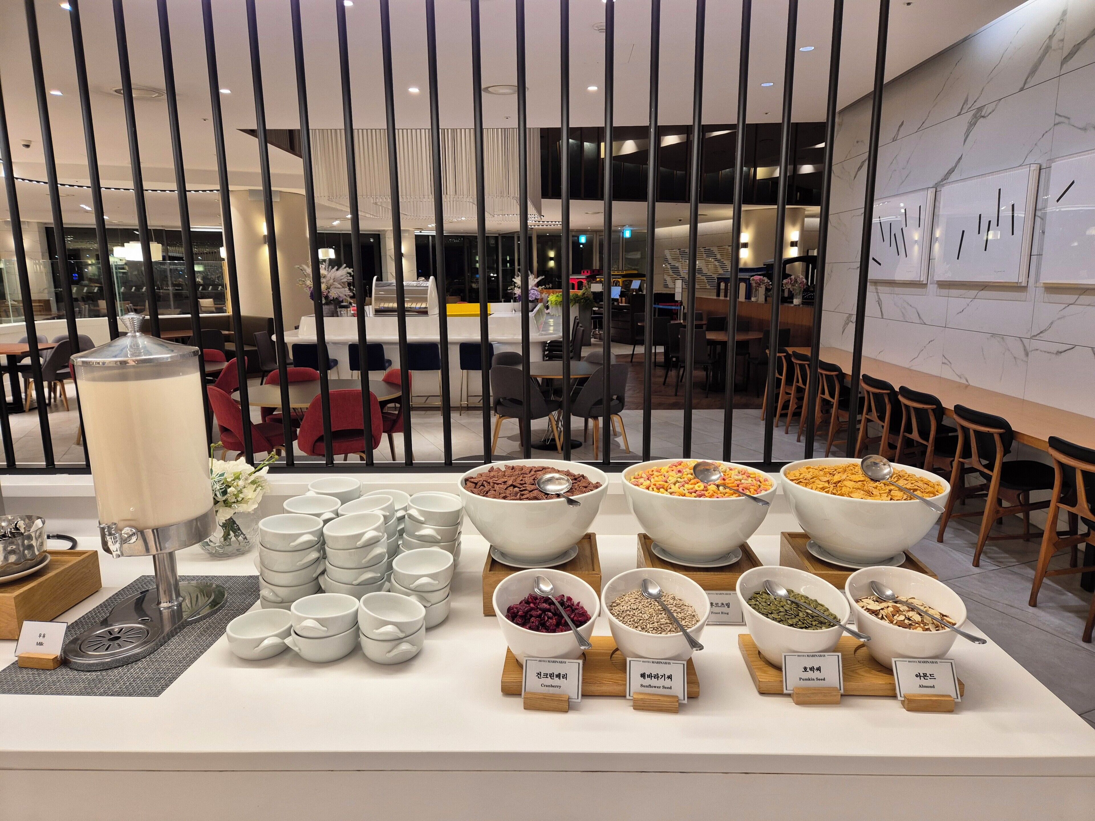 A buffet area with various food options, including bowls of cereal and nuts, and a milk dispenser.