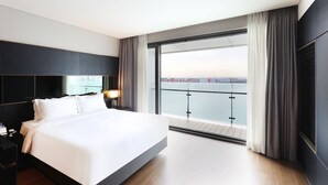 Una habitación de hotel moderna con una cama grande, una mesita de noche, una lámpara y vistas a la ciudad desde un balcón.