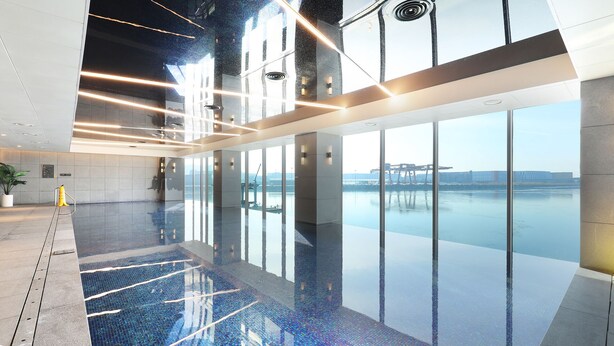 Una piscina interior moderna con techo de vidrio, ventanas amplias y vistas a un puente.