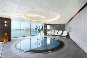 Zona de piscina interior moderna con vista a un puente y edificios al otro lado del agua.