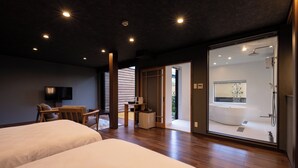 A modern hotel room with two beds, a desk, a chair, a TV, and a glass-enclosed bathroom with a bathtub and shower. - IZUTSURO (Tahara)