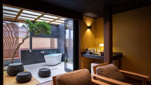 A modern bathroom with a large bathtub, a sink, and a shower area. There are wooden chairs and ottomans in the space. - IZUTSURO (Tahara)