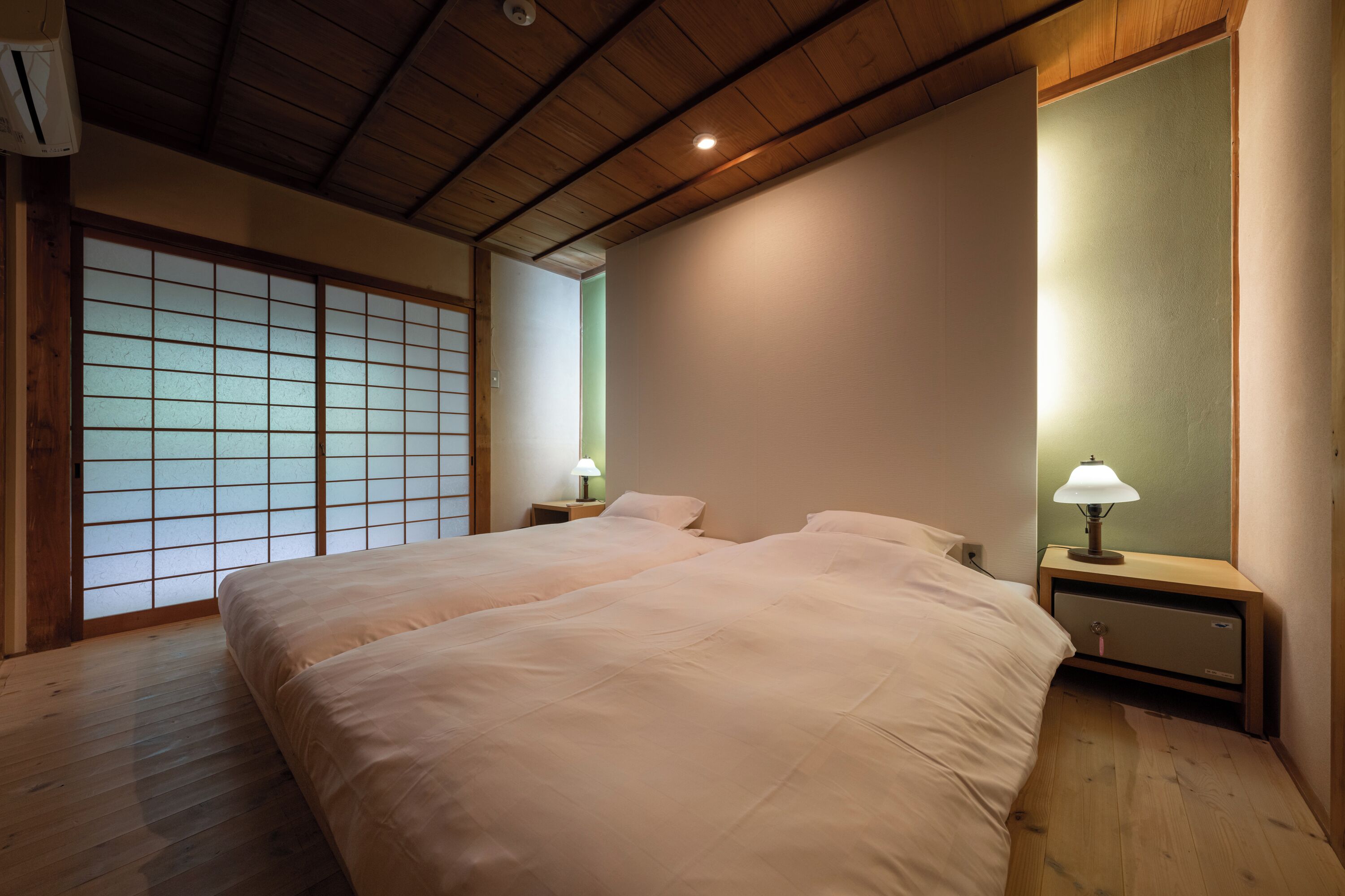 Un dormitorio con dos camas, suelo de madera, un panel shoji y lámparas de noche.