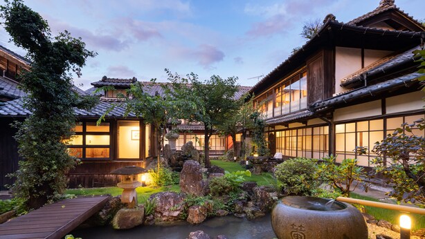 A traditional Japanese courtyard with a koi pond, wooden walkways, and stone lanterns. - IZUTSURO (Tahara)