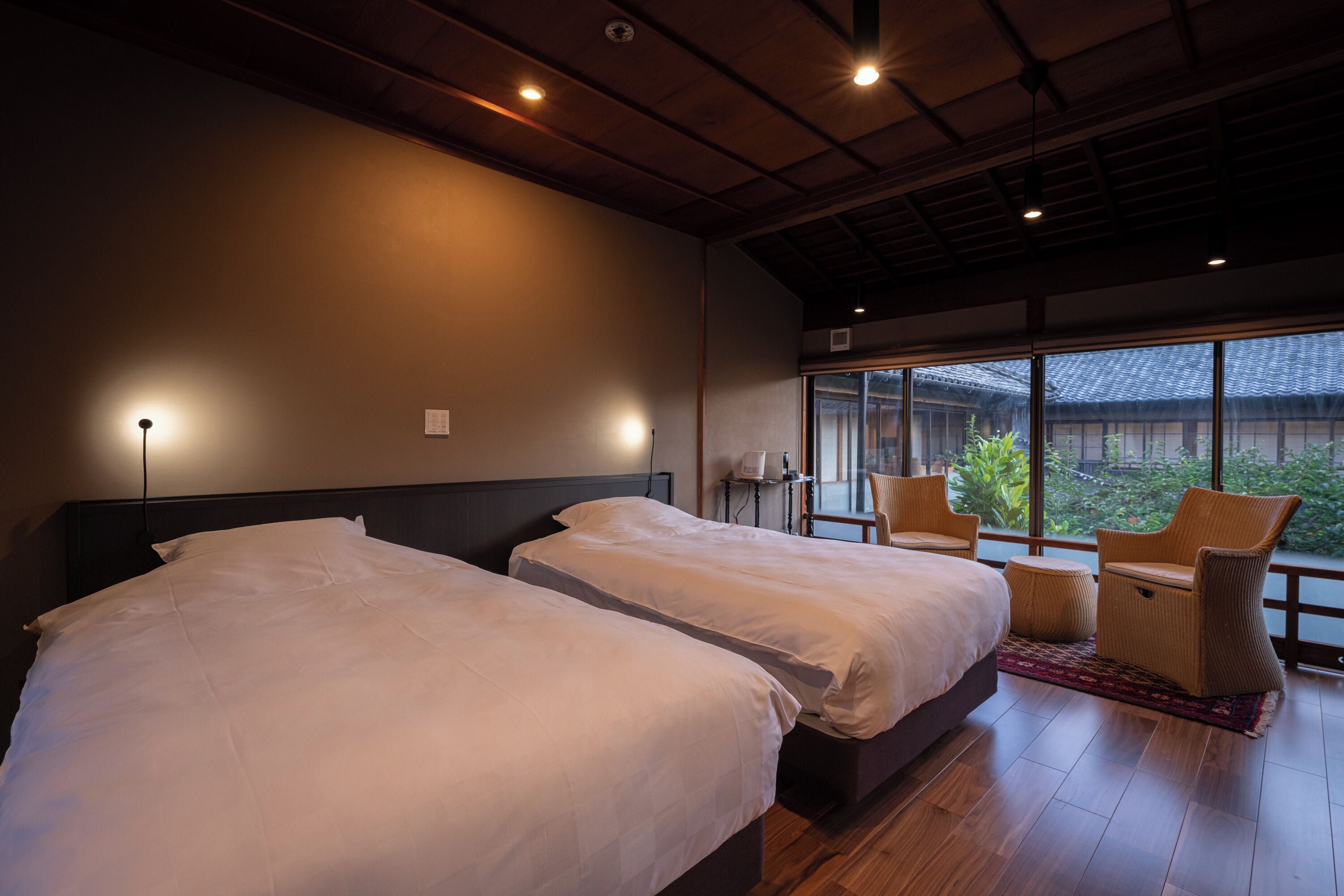 A hotel room with two beds, a large window with a view, and wicker chairs.