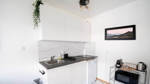 A compact kitchen with white cabinets, a marble backsplash, a sink, a small refrigerator, and a microwave on a metal shelf. - City Loft | 5 Min Rhein-Galerie (Ludwigshafen am Rhein)