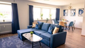 A modern living room with a blue sofa, a coffee table, and a dining area with chairs and a table. - City Loft | 5 Min Rhein-Galerie (Ludwigshafen am Rhein)